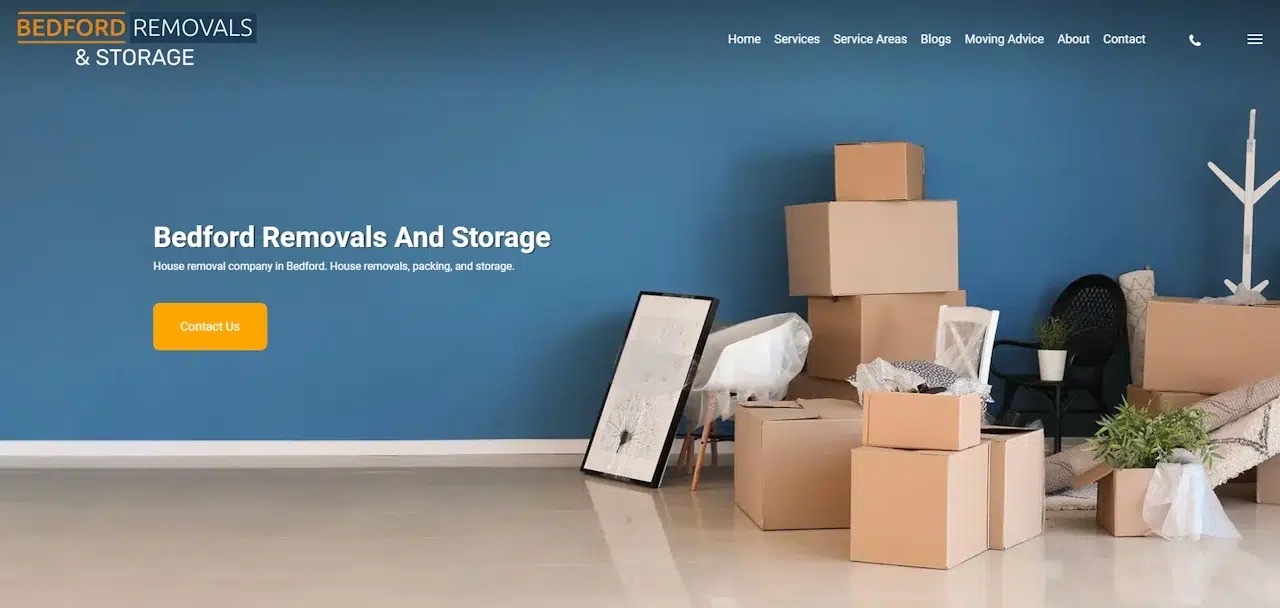 A minimalist room with a blue wall, several packed cardboard boxes, a framed picture, plants, and a standing lamp on the floor. The text reads "Bedford Removals And Storage" and includes a navigation bar with service links and a prominent "Contact Us" button.