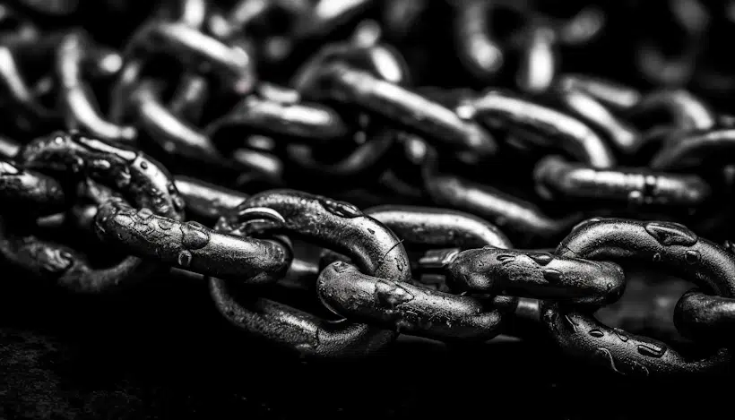 A close-up, black and white photograph of metal chains. The image highlights the texture and details of the intertwined links, showcasing their rugged, worn surface. The background is blurred, emphasizing the focus on the chains in the foreground—much like how backlink monitoring zeroes in on specific link connections.